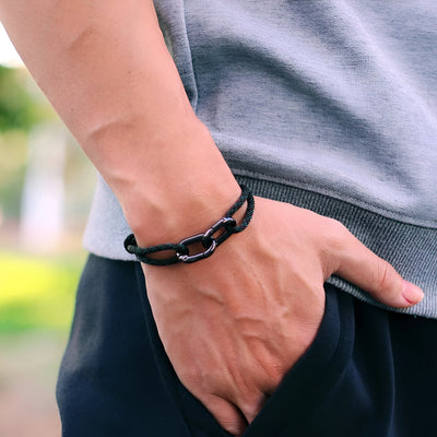 Bracelet cordon noir à double mousquetons pour homme porté au poignet.
