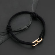 Bracelet cordon noir avec maillons croisés dorés, style moderne et minimaliste.