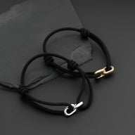 Bracelet cordon noir avec maillon croisé en métal argenté, style ajustable.