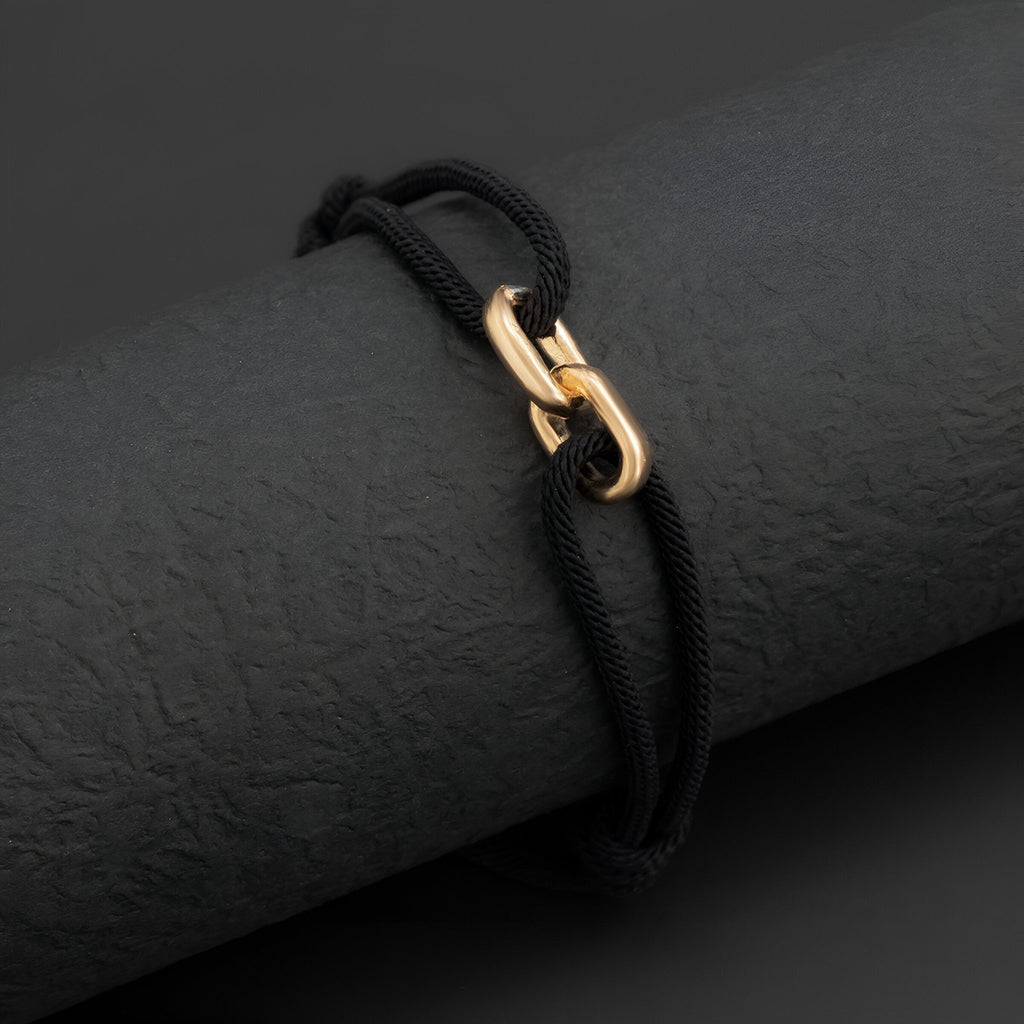Bracelet cordon noir avec maillons croisés en métal doré éclatant.
