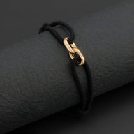 Bracelet cordon noir avec maillons croisés en métal doré éclatant.