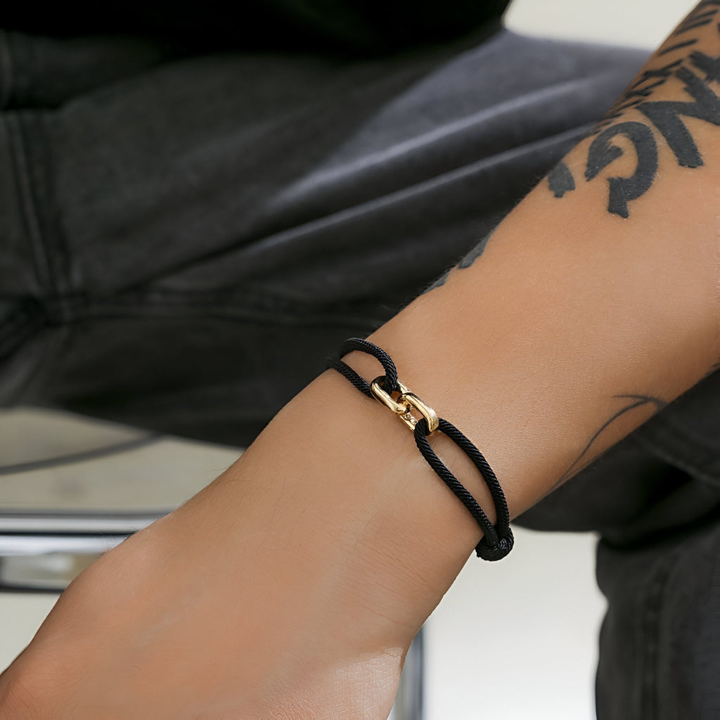 Bracelet cordon noir avec maillon croisé en or, style minimaliste unisexe.