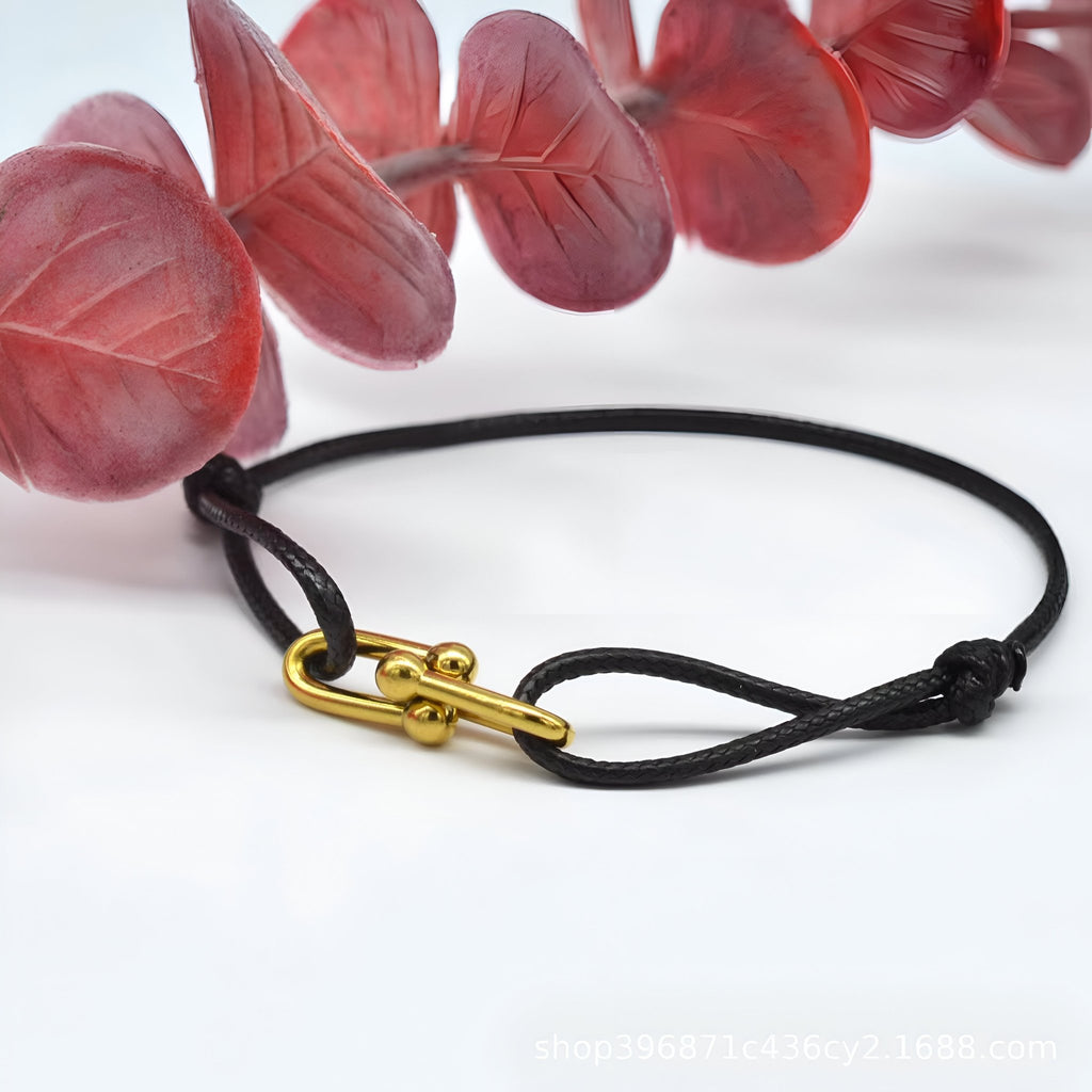 Bracelet cordon noir avec maillon croisé doré élégant, style minimaliste.
