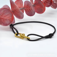 Bracelet cordon noir avec maillon croisé doré élégant, style minimaliste.