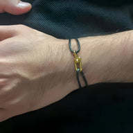 Bracelet cordon noir à double lanière avec maillon doré croisé élégant sur poignet masculin.