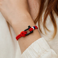 Bracelet cordon rouge à manille noire avec détail rouge et blanc, modèle Elmire, porté au poignet.