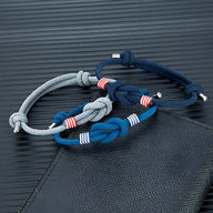 Trois bracelets cordon ajustables en bleu marine, gris et bleu avec nœuds et rayures blanches et rouges.