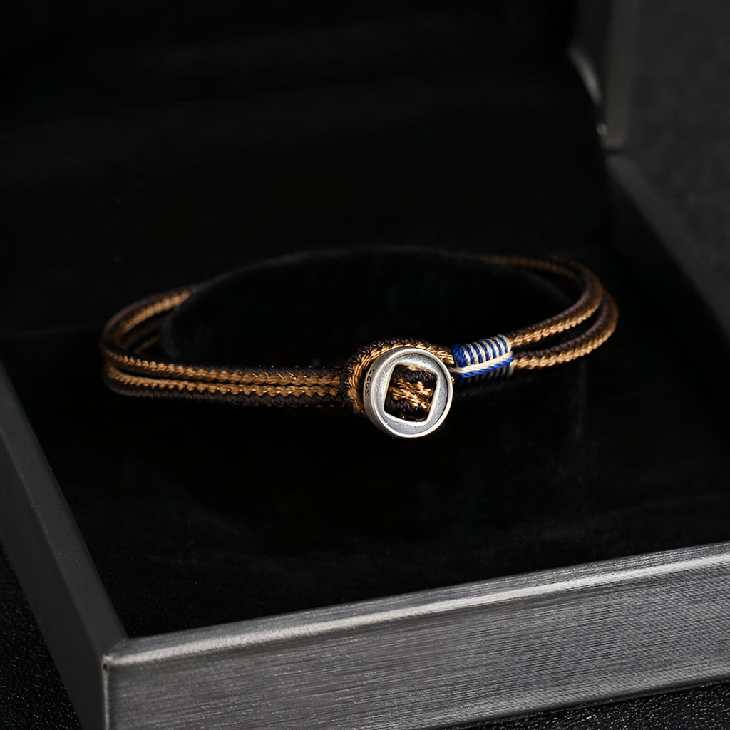 Bracelet cordon marron avec médaillon en argent sterling et détail bleu, élégant et moderne.