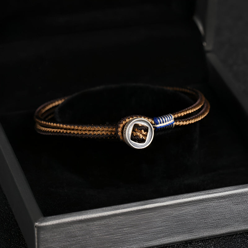 Bracelet cordon marron avec médaillon en argent sterling et détail bleu, élégant et moderne.