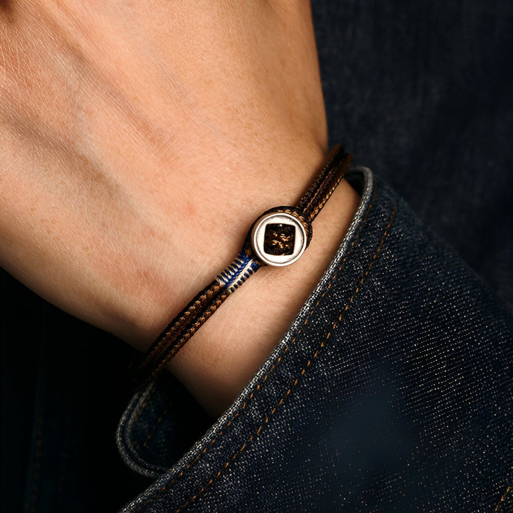 Bracelet cordon marron fin avec plaque centrale en argent sterling portée au poignet.