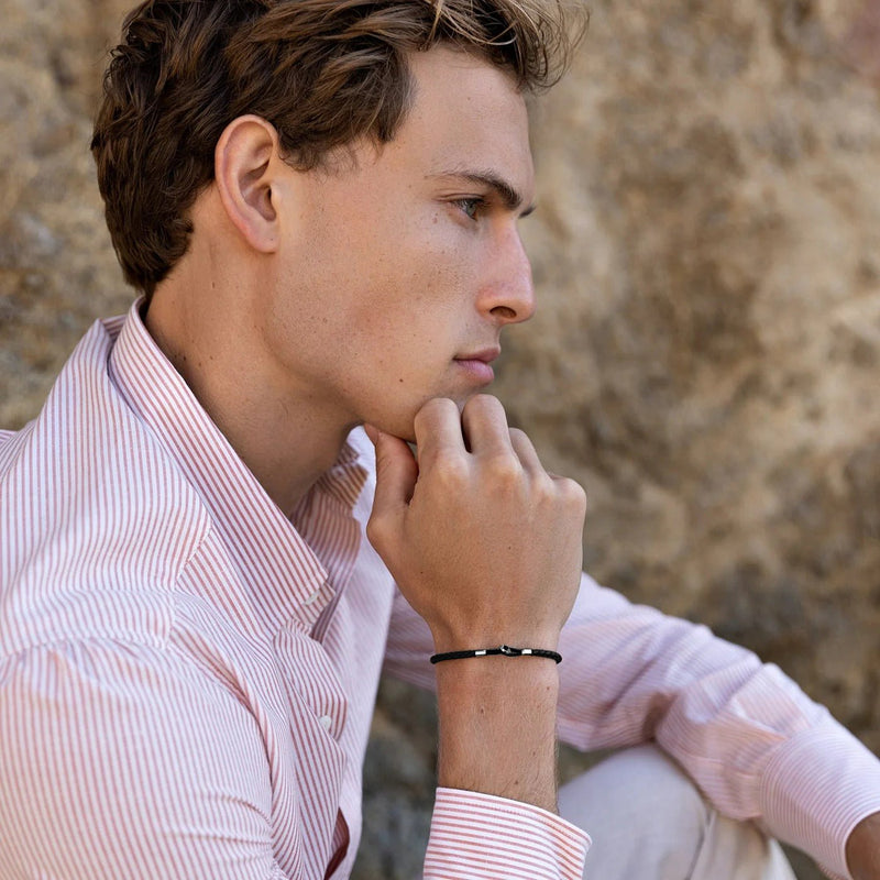 Bracelet cordon noir minimaliste modèle Amadeo porté homme avec chemise rose pâle rayée.