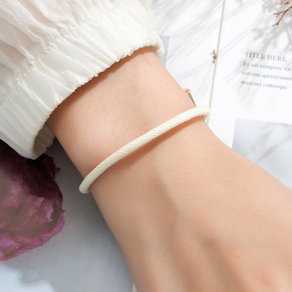 Bracelet cordon crème minimaliste avec détail en titane plaqué or ajusté au poignet.