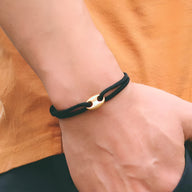 Bracelet cordon noir minimaliste pour homme avec fermoir métallique doré sur poignet.
