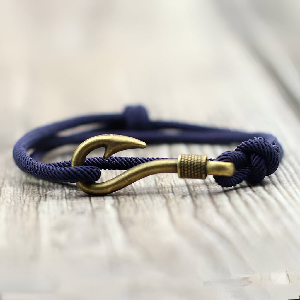 Bracelet cordon bleu marine avec hameçon doré coulissant pour homme sur fond bois.