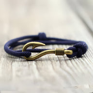 Bracelet cordon bleu marine avec hameçon doré coulissant pour homme sur fond bois.