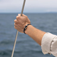 Bracelet cordon double noir à motifs avec mousqueton en acier inoxydable porté au poignet homme.