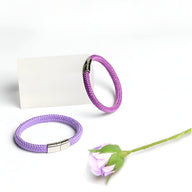 Bracelet cordon violet en corde de bateau avec fermoir acier inoxydable, modèle Elwan, posé avec une fleur lavande claire.