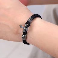 Bracelet cordon noir avec croix chrétienne en acier inoxydable et détails gravés sur poignet.