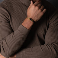 Bracelet cordon cuir noir avec crochet acier inoxydable or, style masculin, porté au poignet.