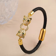 Bracelet en cuir noir tressé avec double tête de guépard dorée ornée de strass verts et blancs.