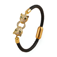 Bracelet cordon noir en cuir avec double tête de guépard dorée ornée de pierres vertes et blanches.