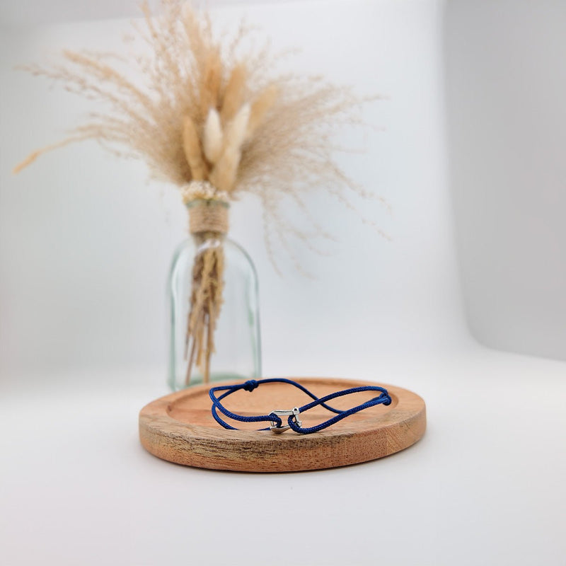 Bracelet cordon bleu marine avec pendentif en forme de fer à cheval en acier inoxydable sur plateau rond en bois clair.