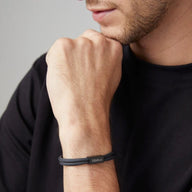 Bracelet cordon noir avec plaque en acier inoxydable gravée, style discret et moderne, porté au poignet masculin.