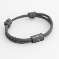 Bracelet cordon gris avec plaque en acier inoxydable gravée des prénoms Markus et Ella, fermeture ajustable.