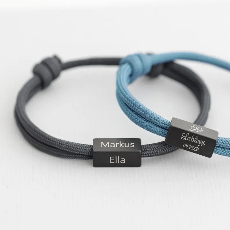 Bracelet cordon noir avec plaque acier inoxydable gravée "Markus Ella" et bracelet cordon bleu clair avec plaque gravée.
