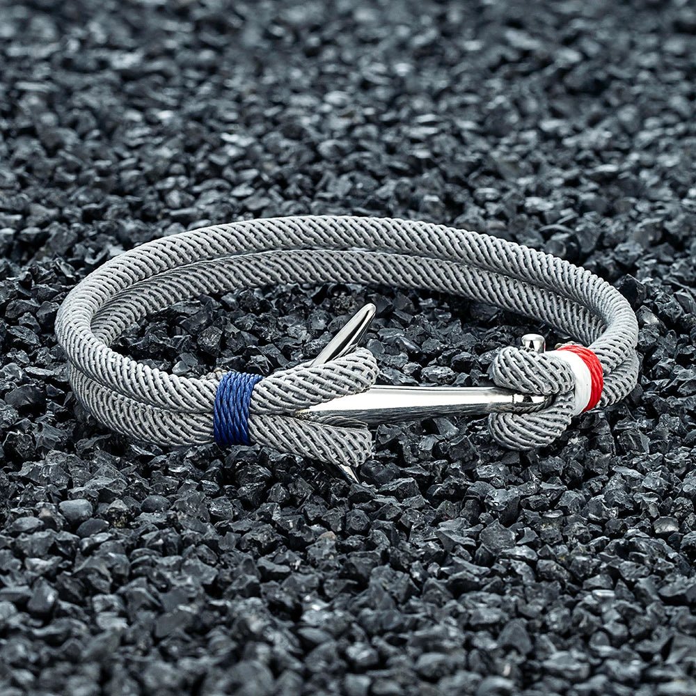 Bracelet cordon gris tressé avec ancre argentée en acier inoxydable et détails bleu et rouge.