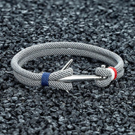 Bracelet cordon gris tressé avec ancre argentée en acier inoxydable et détails bleu et rouge.