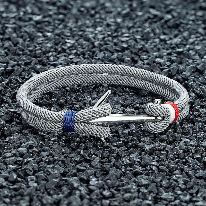 Bracelet cordon gris tressé avec ancre argentée en acier inoxydable et détails bleu et rouge.