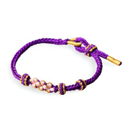 Bracelet cordon violet avec perles blanches à motif floral et détails dorés.