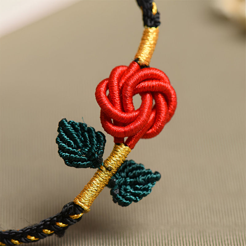 Bracelet cordon noir avec motif rose rouge nouée et deux feuilles vertes brodées, détails dorés.