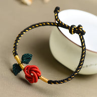 Bracelet cordon noir avec motif rose rouge et feuilles vertes, détails dorés élégants.