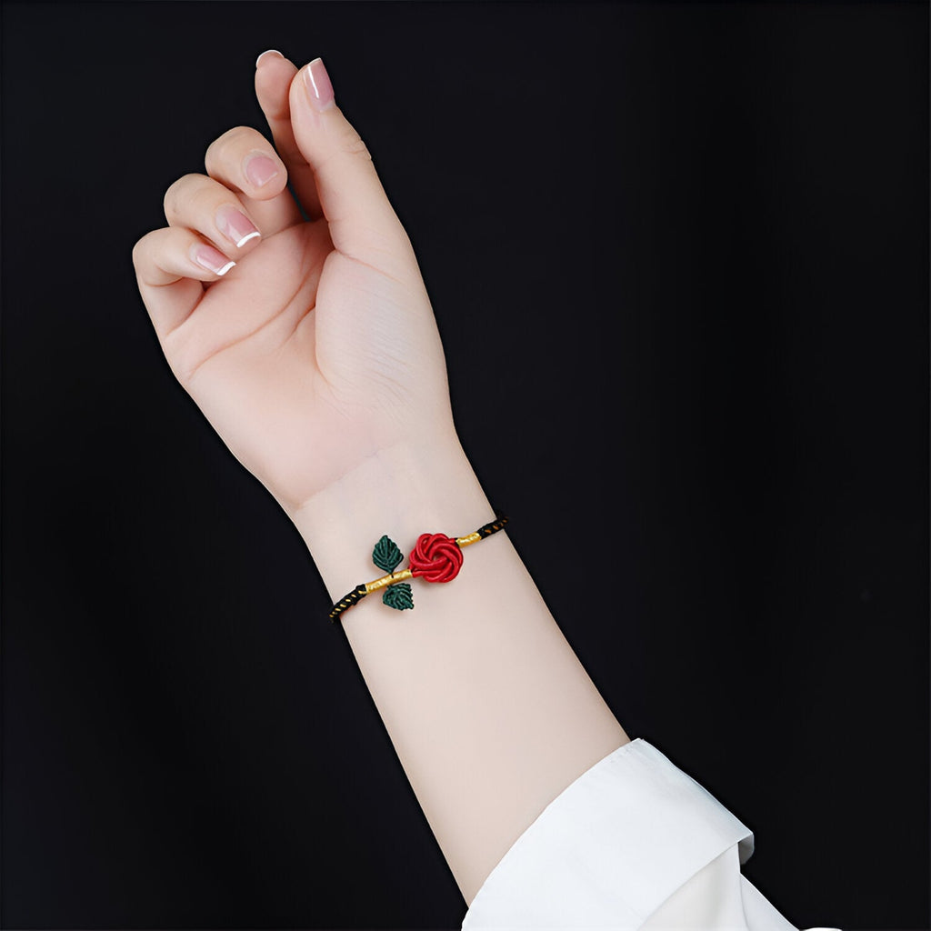 Bracelet cordon noir avec motif rose rouge et feuilles vertes porté au poignet féminin.