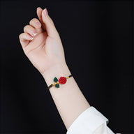 Bracelet cordon noir avec motif rose rouge et feuilles vertes porté au poignet féminin.