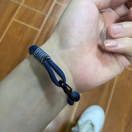 Bracelet cordon bleu avec noeud et petit mousqueton noir porté au poignet.