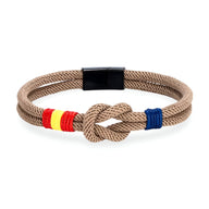 Bracelet cordon beige avec nœud et drapeau espagnol en fil rouge et jaune, détail bleu, fermoir noir.