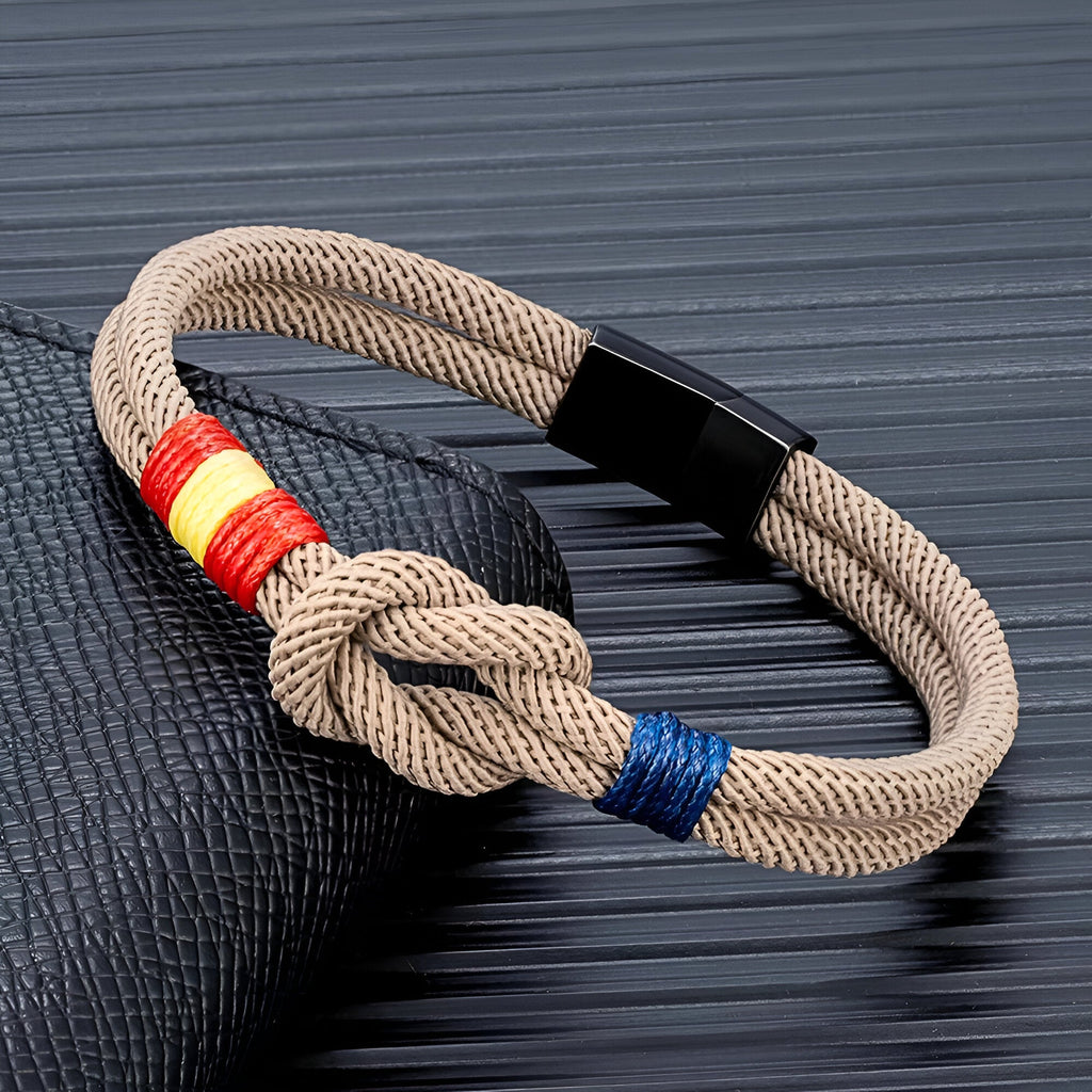 Bracelet cordon beige avec nœud et détails aux couleurs du drapeau espagnol, fermoir noir brillant.