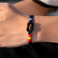 Bracelet cordon noir avec nœud et drapeau espagnol en rouge et jaune sur poignet.