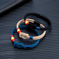 Lot de bracelets cordon en beige, noir et bleu, avec nœud et détails couleur drapeau espagnol.
