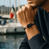 Bracelet cordon bleu marine avec noeud, détail drapeau français en tissu rouge, blanc et bleu, porté au poignet masculin.