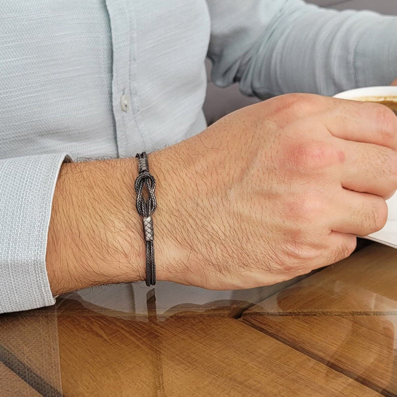 Bracelet cordon gris avec nœud en argent sterling 925 porté au poignet homme avec chemise bleue.