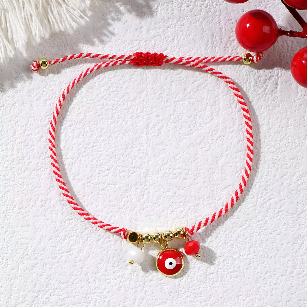 Bracelet cordon rouge tressé avec pendentifs œil de dzi, perle blanche et détails dorés.