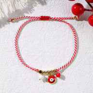 Bracelet cordon rouge tressé avec pendentifs œil de dzi, perle blanche et détails dorés.