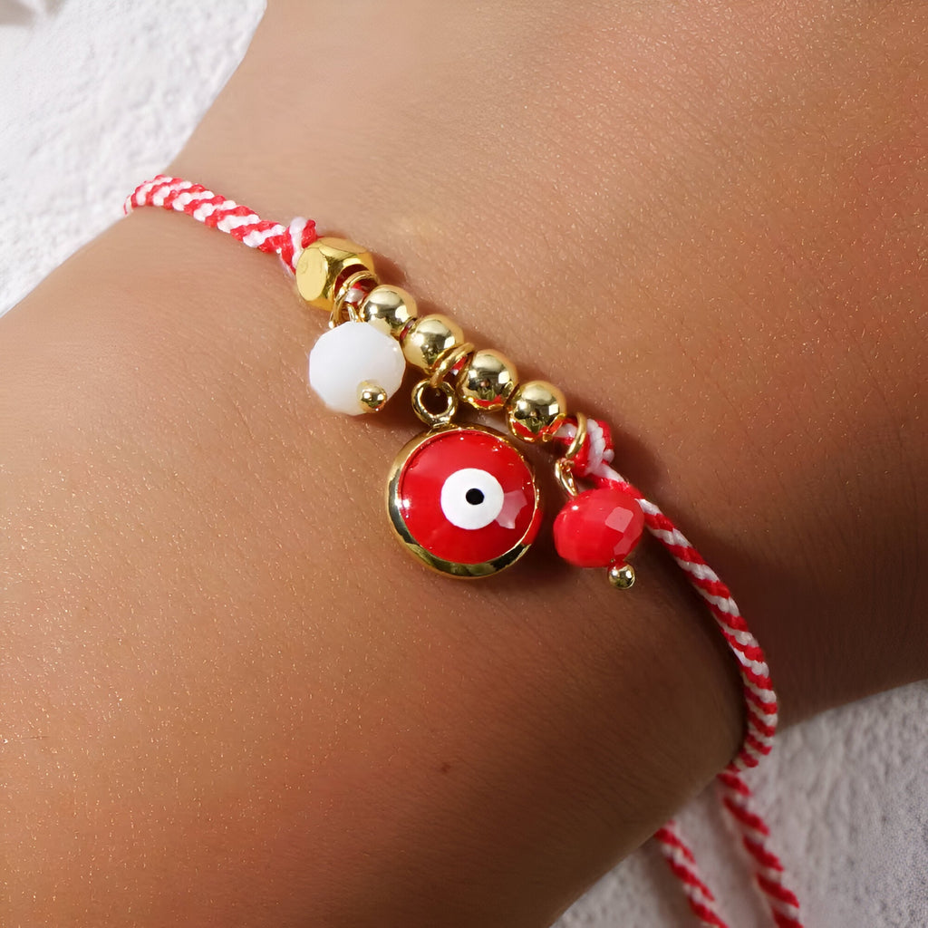 Bracelet cordon rouge avec perles dorées et pendentif œil de dzi rouge sur poignet féminin.