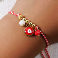 Bracelet cordon rouge avec perles dorées et pendentif œil de dzi rouge sur poignet féminin.