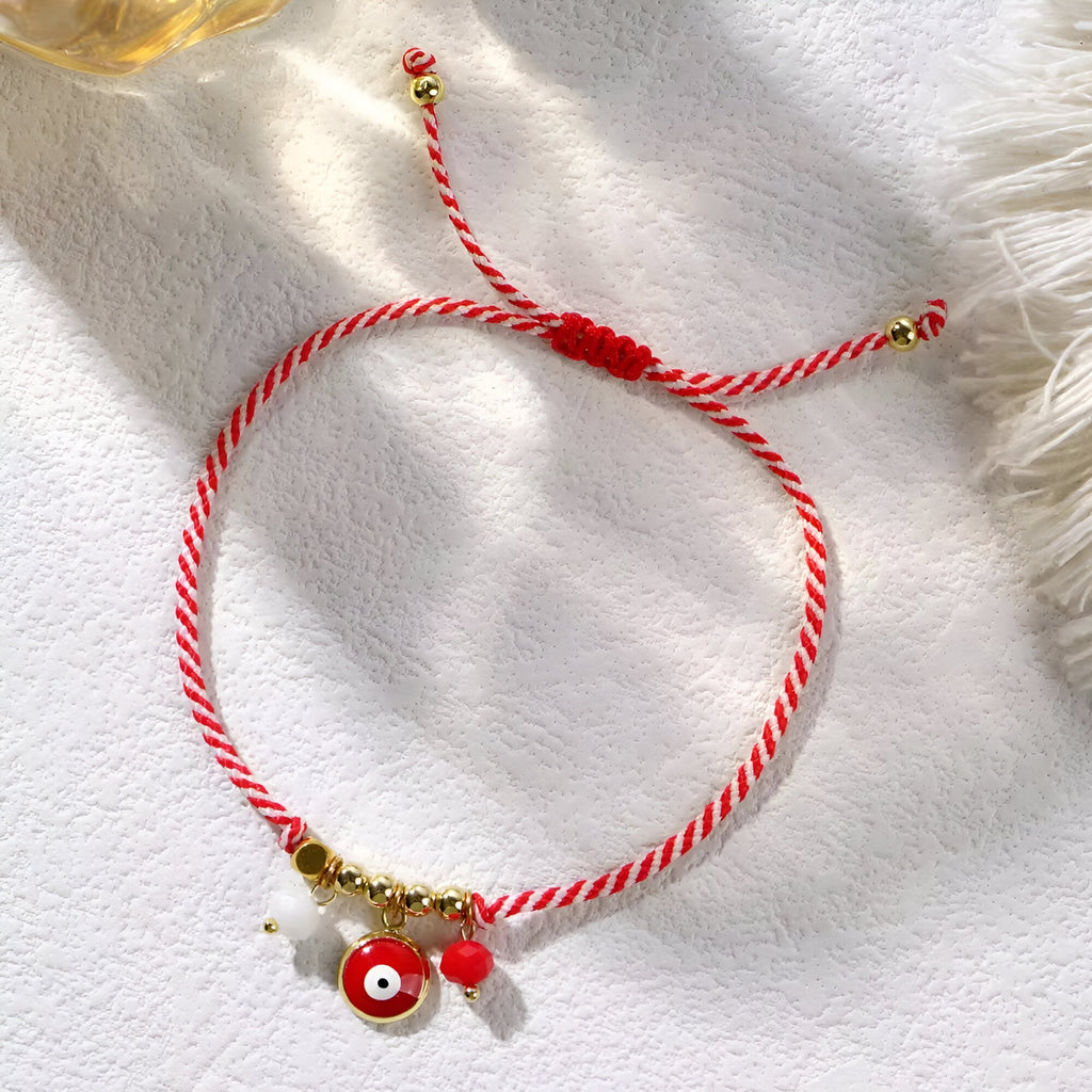 Bracelet cordon rouge tressé avec pendentifs œil de Dzi, perles dorées et décorations rouges.