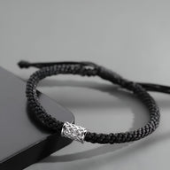 Bracelet cordon noir tressé avec ornement cylindrique en argent au design gravé.